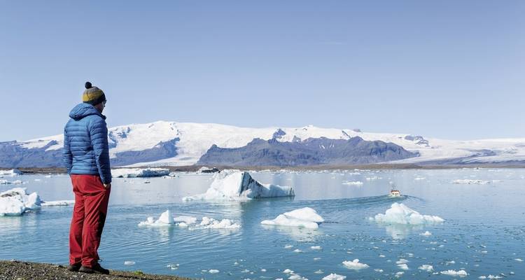Person in Winterkleidung, die Eisberge auf einem ruhigen See betrachtet.