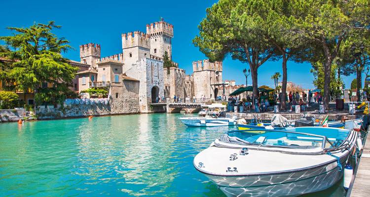 A picturesque castle by the water with boats and people bustling around.