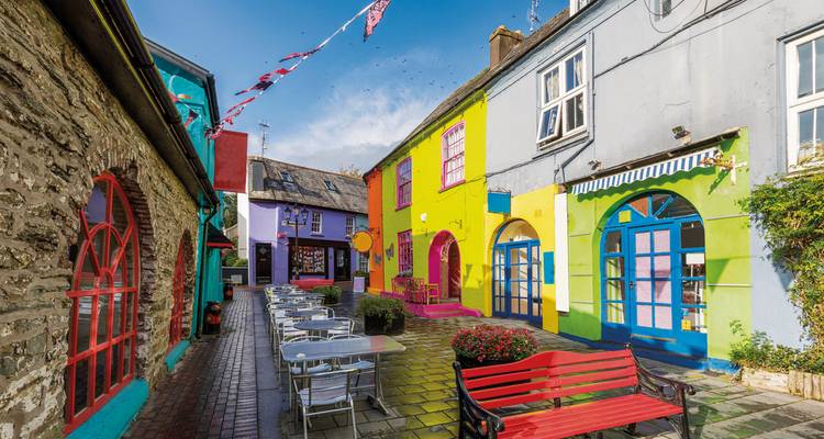 Lebendige, farbenfrohe Gasse mit Cafés, Bänken und Wimpelketten in der Küstenstadt Kinsale.