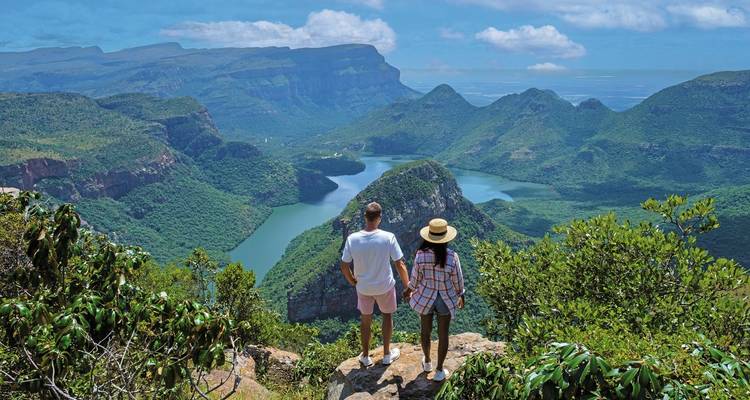 Twee mensen die uitkijken over een weelderige vallei en rivier vanaf een klif.