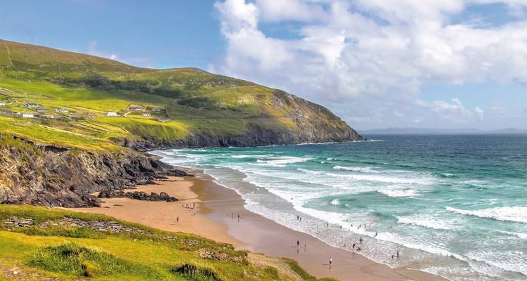 Plage de sable fin avec des vagues turquoise qui roulent contre des falaises verdoyantes tandis que les visiteurs jouent le long du rivage.