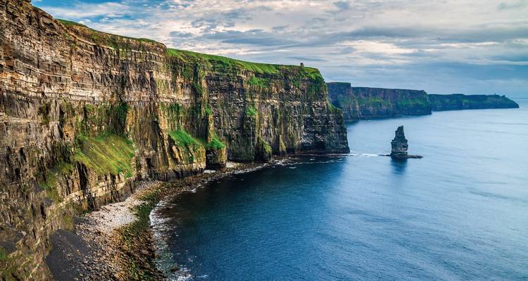 Steep sea cliffs stretch into the distance, their layered rock faces capped with bright green grass.