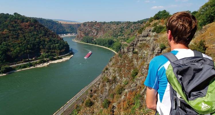 Un randonneur surplombant un méandre de rivière avec un bateau qui passe.