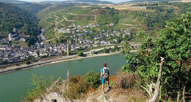 Un randonneur contemplant un village de l'autre côté d'une rivière depuis le sommet d'une colline.
