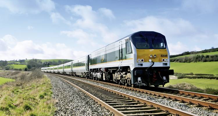 Passenger train traversing through a lush green Irish landscape.