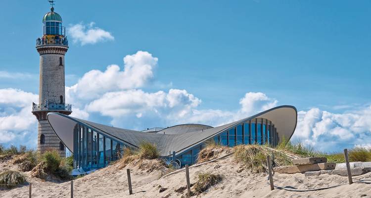 Modern seaside building with a lighthouse against a blue sky.