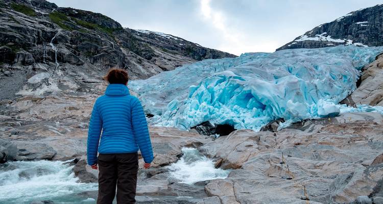Eine Person, die einen Gletscher mit fließendem Wasser in einer rauen Landschaft betrachtet.