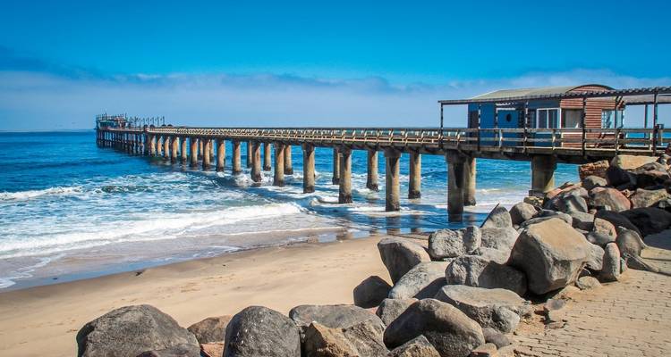 Pier extending into the ocean with waves crashing on rocks.