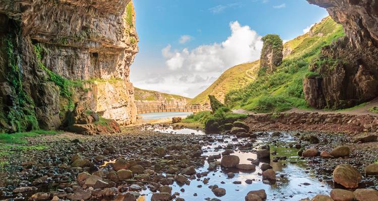 Cave entrance with a stream leading to the sea, surrounded by rocky cliffs.