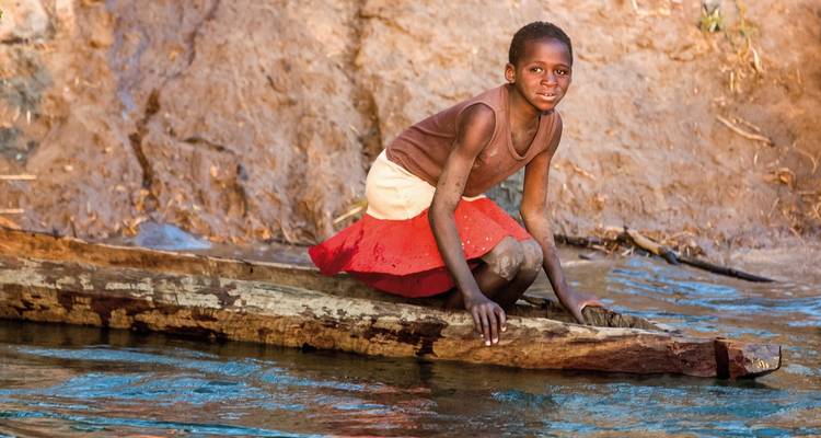 Child playing on a wooden log in a river.