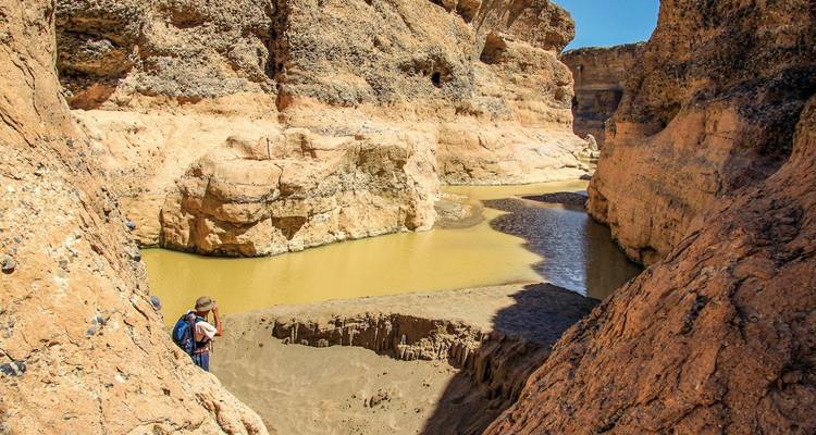 Person exploring a narrow, rocky canyon with a small river.