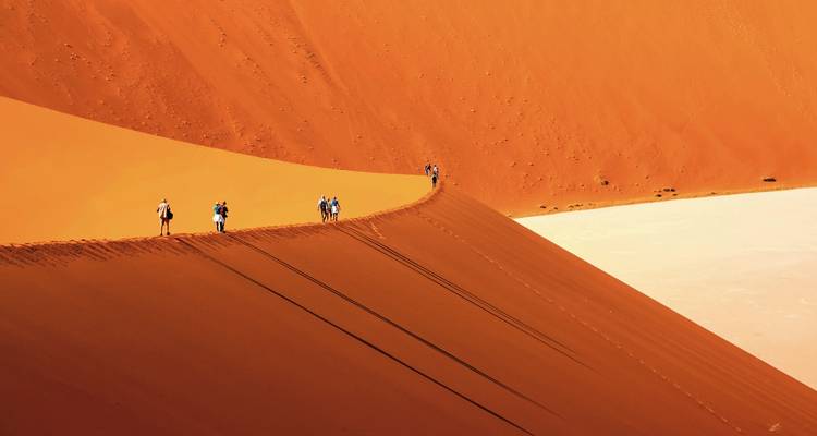 Tourists walking on a massive red sand dune under a clear sky.