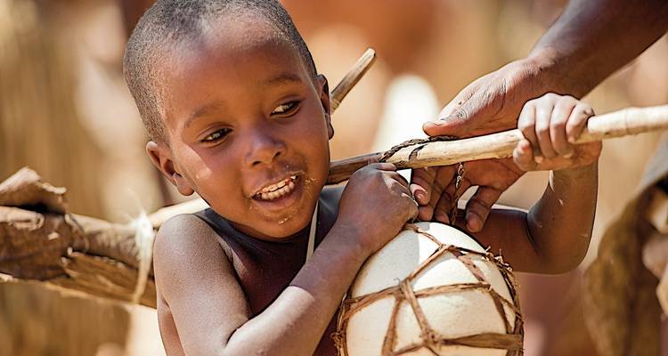 Child carrying a woven basket with a stick.