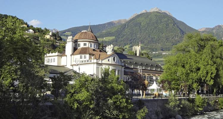 Historisches Gebäude inmitten üppigen Grüns mit Bergkulisse.