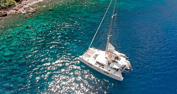 Aerial view of a sailboat on clear blue ocean water.