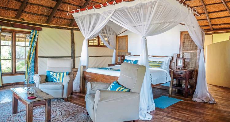 Innenraum einer Luxuslodge mit einem Bett und Stühlen.