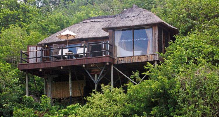 Erhöhte Unterkunft mit Strohdach, umgeben von üppigem Grün.