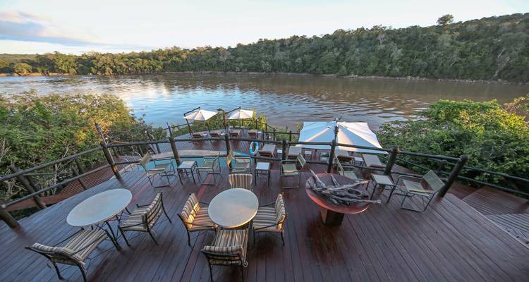 Terrassenbereich mit Blick auf einen Fluss mit Stühlen und Sonnenschirmen.