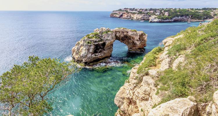 Arche rocheuse naturelle au-dessus d'eaux turquoise avec falaises et végétation.