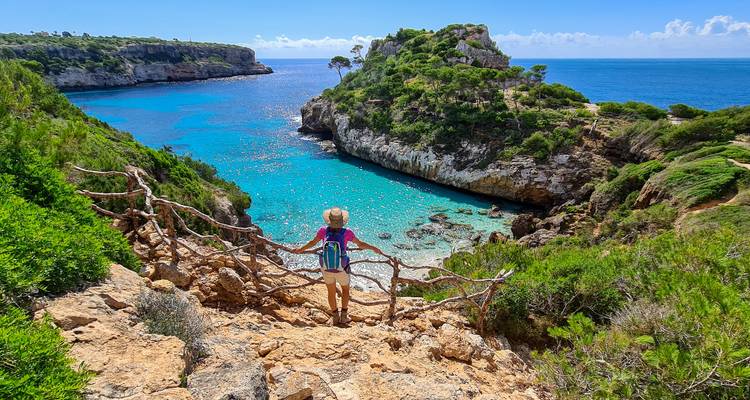 Person, die auf einem Felsvorsprung steht und auf klares blaues Wasser blickt.