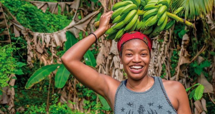 Persoon die glimlacht terwijl hij bananen vasthoudt in een tropische omgeving.