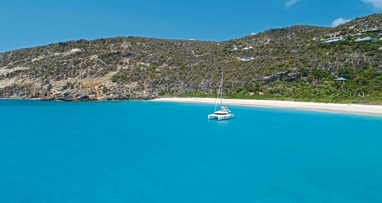 Ein ruhiger Strand mit einer Yacht, die in Küstennähe vor Anker liegt.
