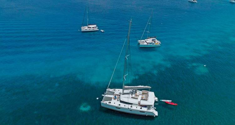 Luftaufnahme von Yachten, die in klarem, blauem Wasser vor Anker liegen.
