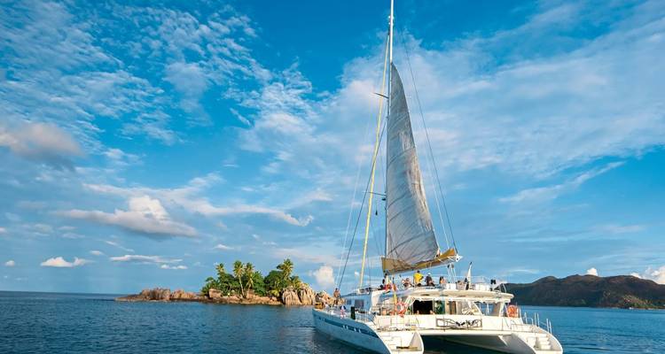 Un yacht avec les voiles hissées près d'une petite île sous un ciel dégagé.