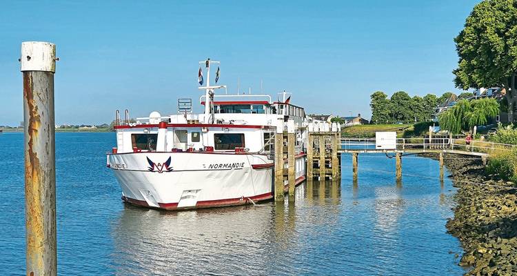 Un bateau de croisière fluviale amarré le long d'une jetée en bois par une journée ensoleillée.
