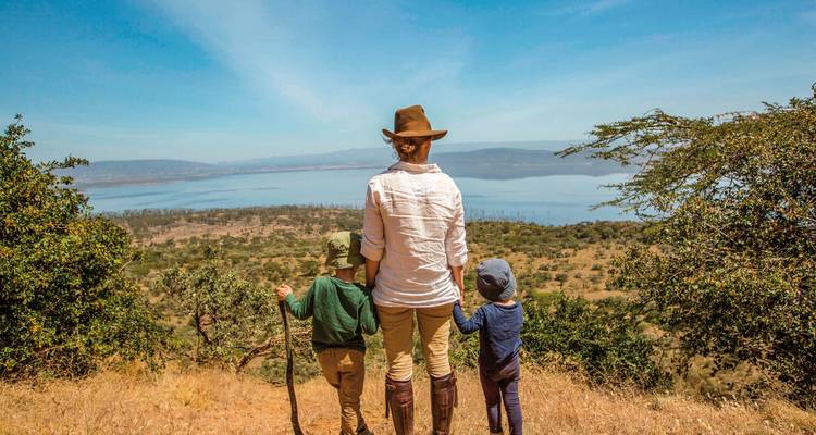 Person mit zwei Kindern mit Blick auf einen See mit Bergen im Hintergrund