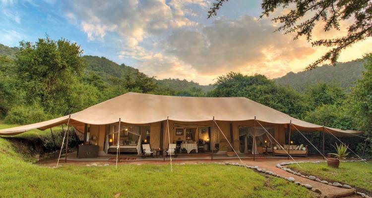 Luxe tent in een weelderige omgeving met bomen en bergen.