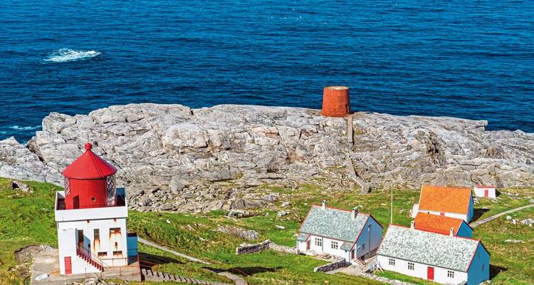 Küstenleuchtturm und Gebäude an felsiger Küste.