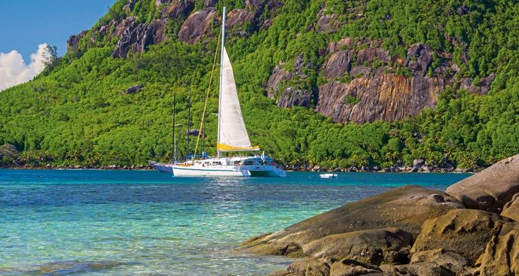 Ein Katamaran segelt in der Nähe einer üppigen Insel auf den Seychellen.