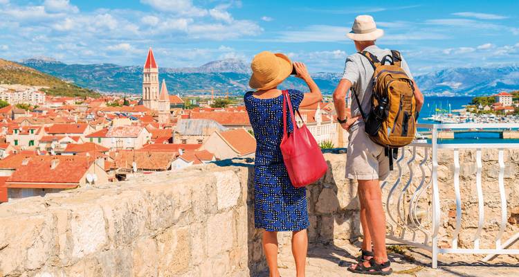 View of tourists enjoying a lookout over a coastal city with red-roofed buildings.