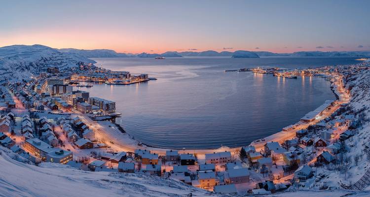 Vue panoramique d'une ville portuaire enneigée sous un ciel coloré au crépuscule.