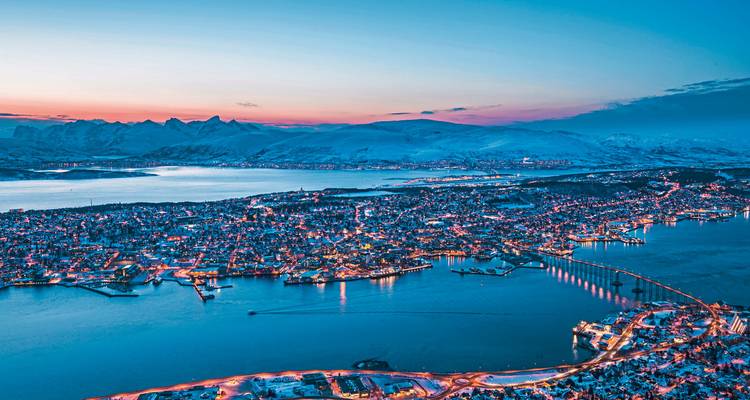Vue aérienne d'une ville au crépuscule avec des montagnes enneigées et l'océan.