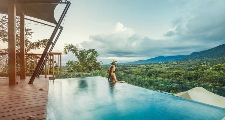 Une personne dans une piscine à débordement surplombant un vaste paysage de forêt verdoyante.
