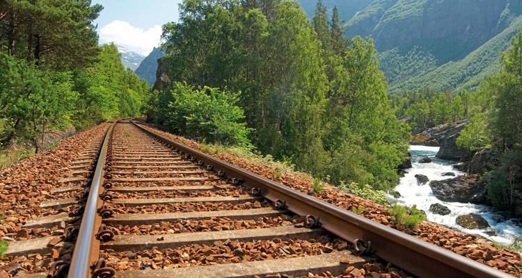 Railroad tracks through a green landscape with mountains.