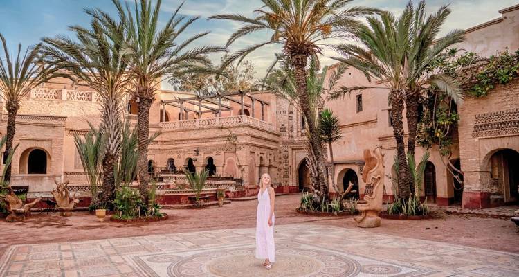 A woman in a courtyard with palm trees and traditional buildings.
