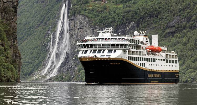 Navire de croisière passant devant une cascade dans un fjord luxuriant.