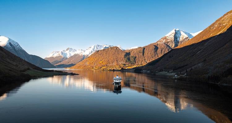 Navire de croisière naviguant dans un fjord calme avec des sommets enneigés.
