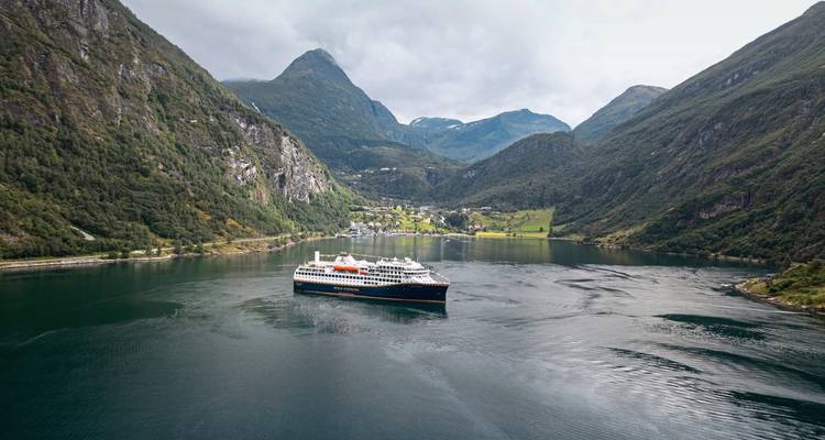 Navire de croisière dans un fjord avec des montagnes et des villages en arrière-plan.