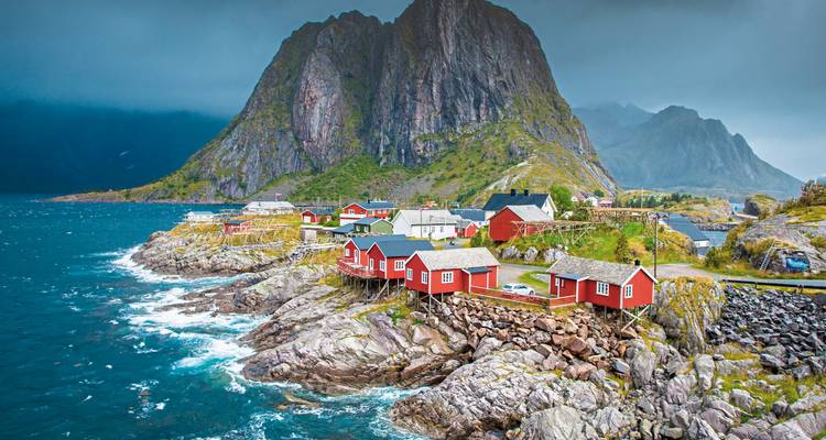 Maisons rouges traditionnelles sur un paysage côtier rocheux avec des montagnes.