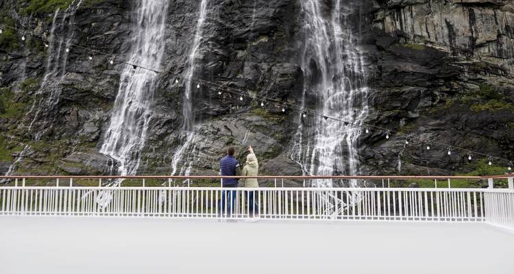 Les voyageurs sur le pont lèvent les yeux vers des chutes d'eau spectaculaires qui dévalent sur la roche sombre.