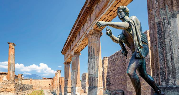 Ruines antiques avec une statue de bronze proéminente se détachant sur un ciel bleu.