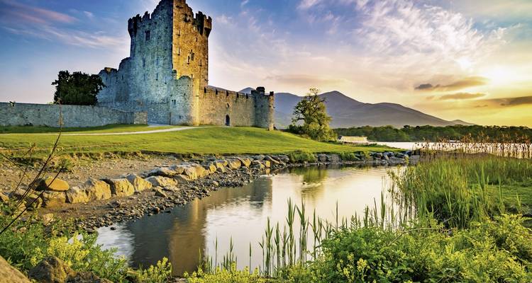 Château historique au bord d'un lac tranquille au coucher du soleil.