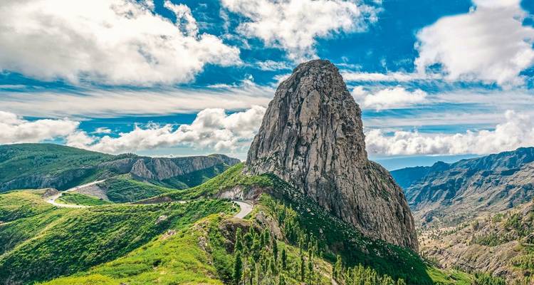 Un pico rocoso prominente con caminos serpenteantes y montañas al fondo.