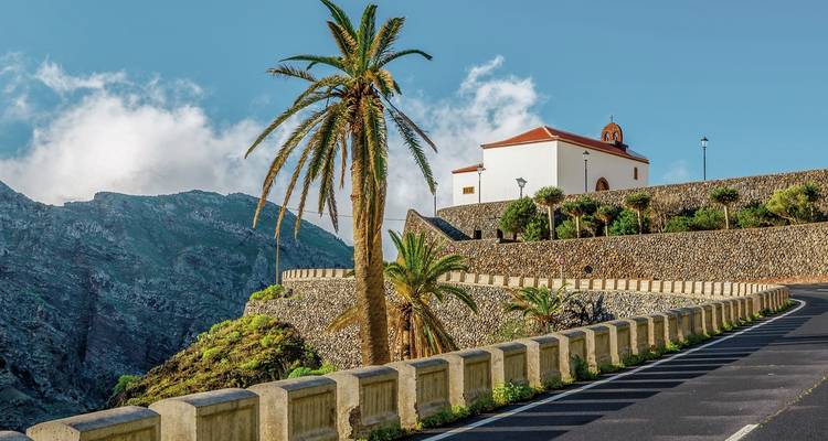 Camino que lleva a una pequeña iglesia con montañas al fondo.