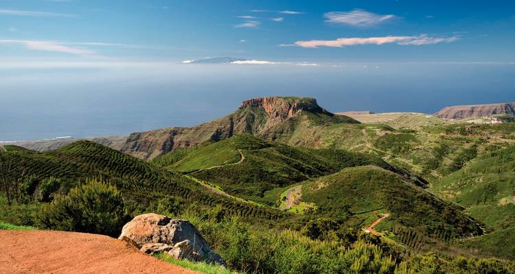 Vasto paisaje verde con una cordillera bajo un cielo despejado.