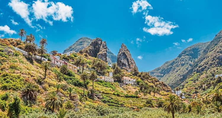 Pueblos y campos en terrazas en una ladera verde de montaña bajo un cielo azul.